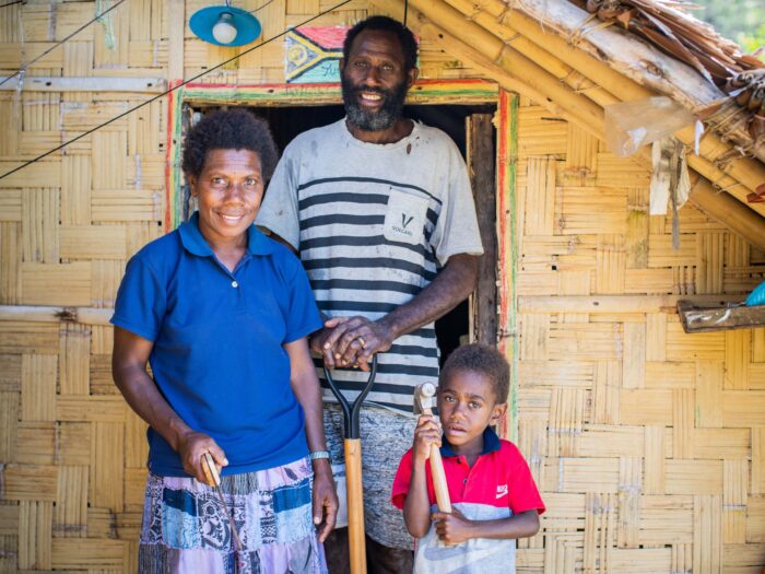 A family stand in front of their Vanuatu home holding tools