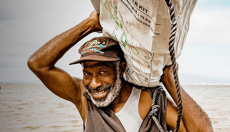 Man carrying shelter kit next to sea in Vanuatu
