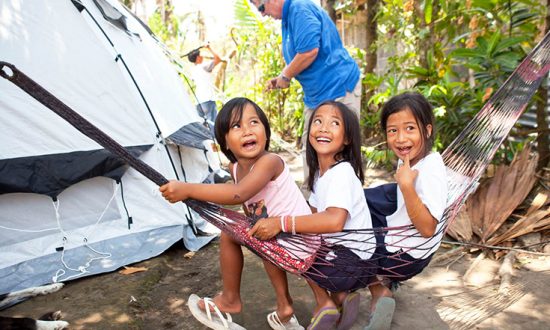 3 children sitting in a hammock next to a tent in the Philippines